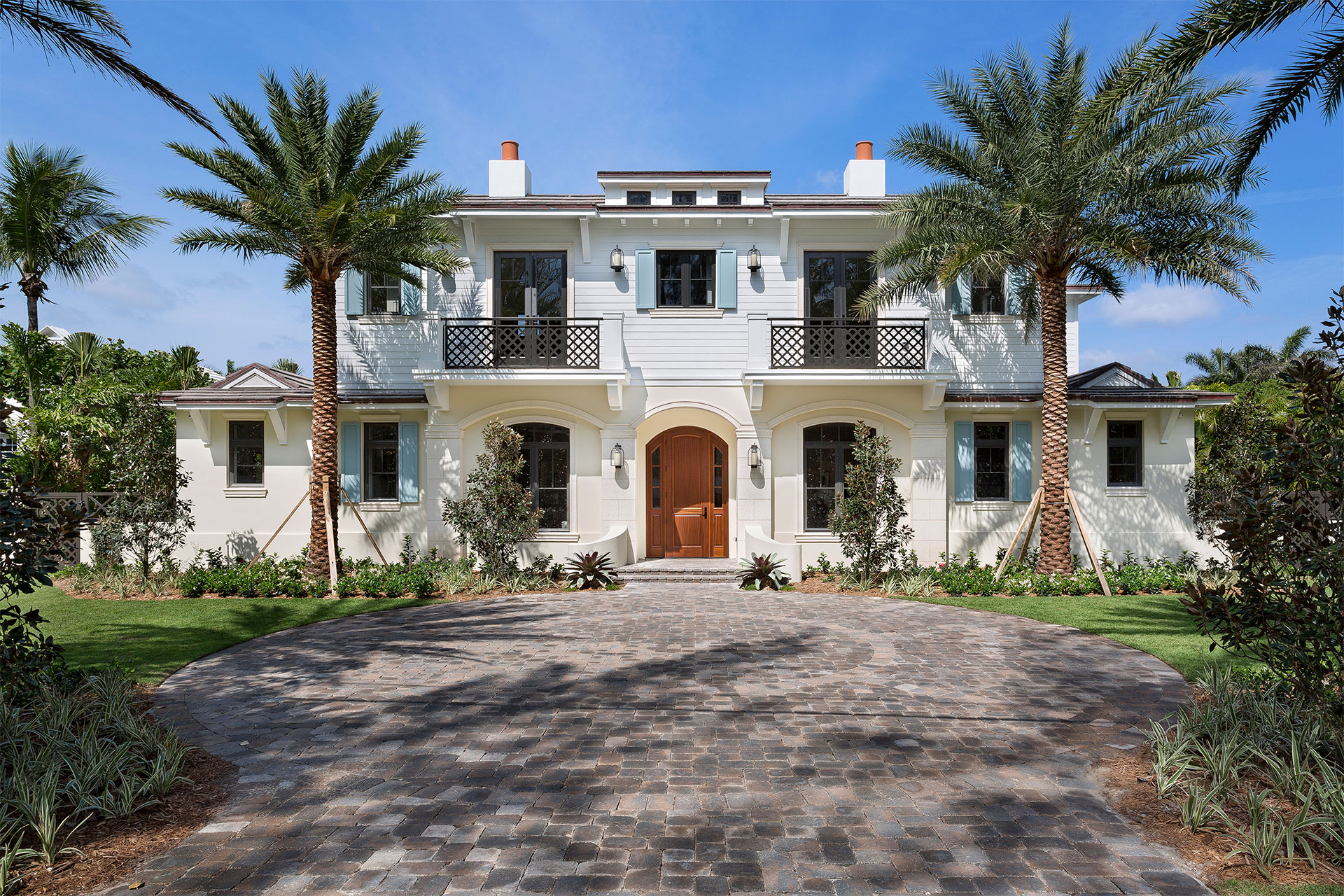 2 story white island-inspired estate with two palm trees in front of it